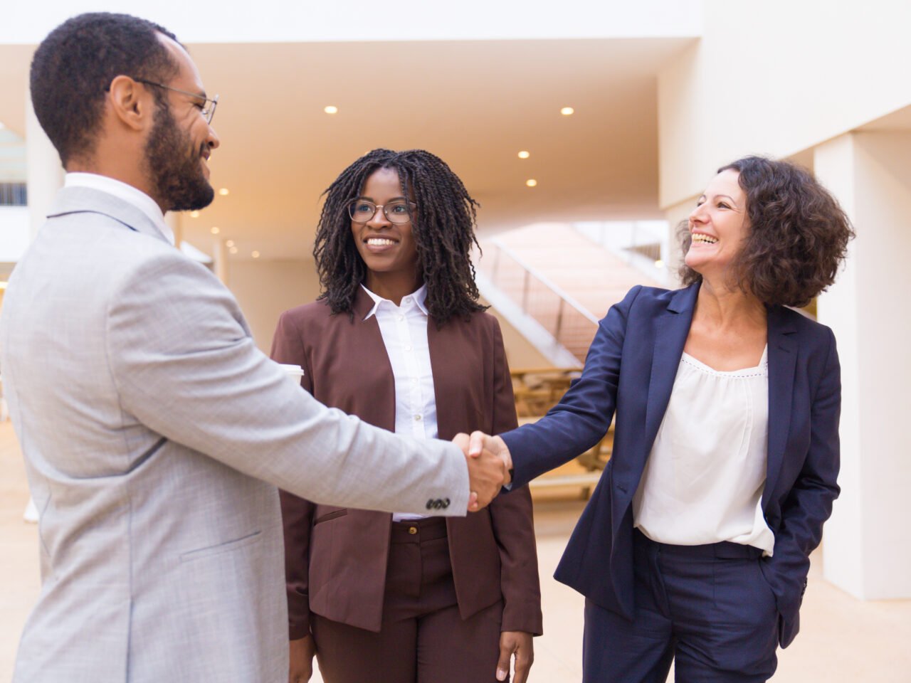 Happy business partners greeting each other. Business man and women standing in office hallway, shaking hands, smiling, talking. Business communication concept