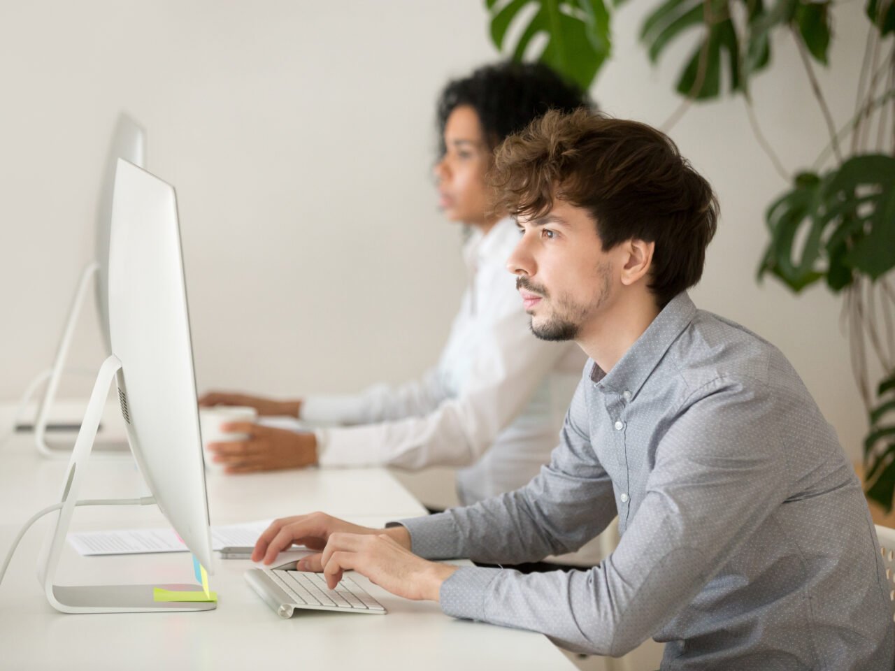 Young employee focused on computer in multiracial shared office, serious guy programmer or web designer using pc corporate software for daily tasks, company manager working  online on desktop